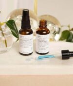 To små flasker fra Evolve Hydrate & Soothe Bundle på en badeværelsesdisk med en dråbe og botaniske dekorationer i baggrunden.