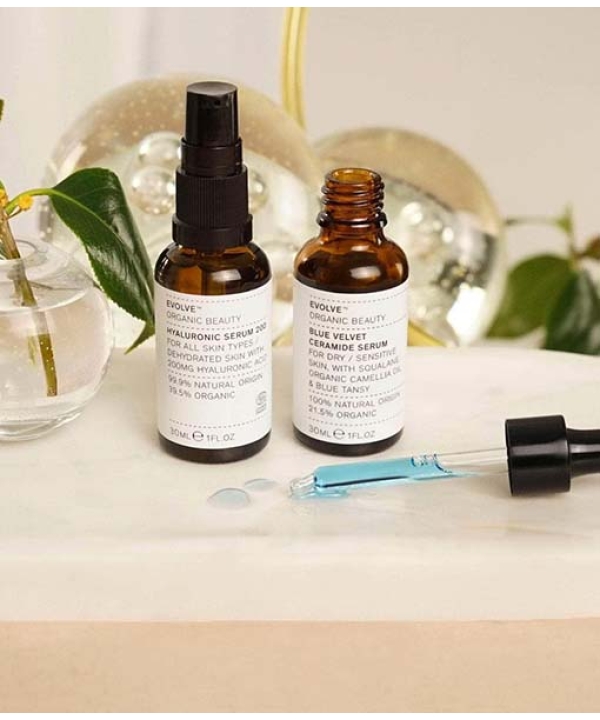 To små flasker fra Evolve Hydrate & Soothe Bundle på en badeværelsesdisk med en dråbe og botaniske dekorationer i baggrunden.