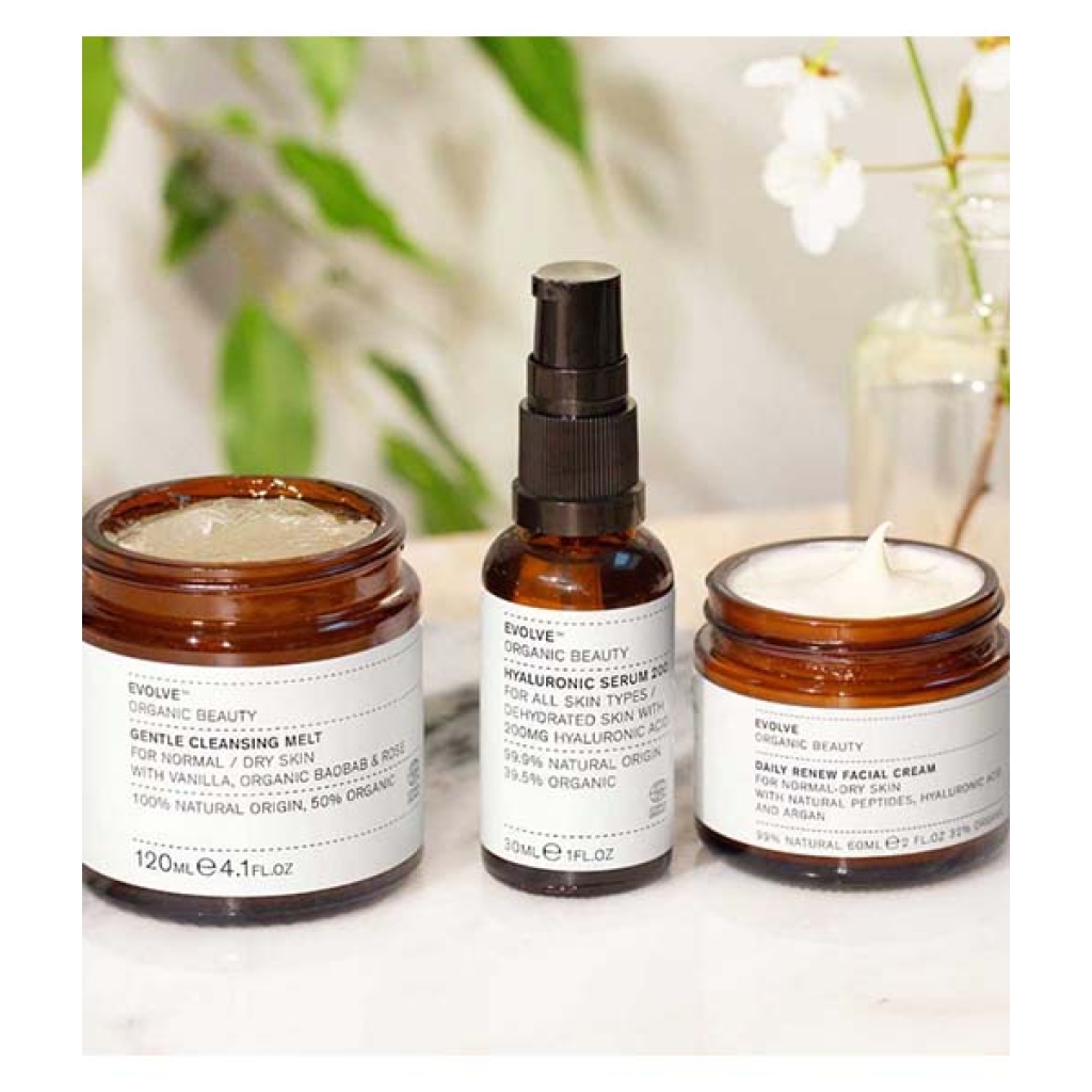 Tre krukker med Caudalie Evolve Hydration Trio Bundle hudplejeprodukter på en marmoroverflade med hvide blomster i baggrunden.