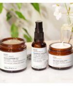 Tre krukker med Caudalie Evolve Hydration Trio Bundle hudplejeprodukter på en marmoroverflade med hvide blomster i baggrunden.