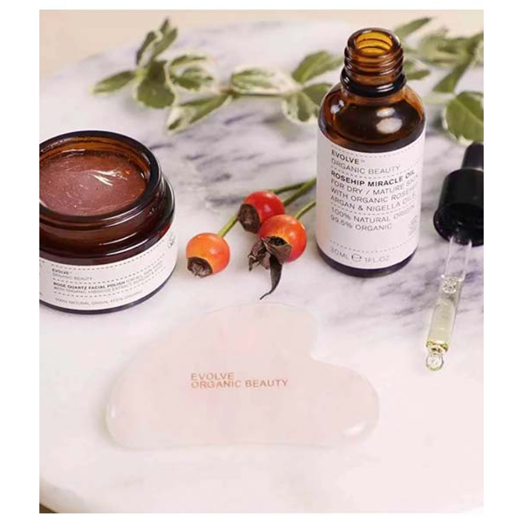 Økologiske hudplejeprodukter, inklusive en krukke med ansigtsmaske, en flaske serum, et gua sha-værktøj og Evolve Love Your Skin Trio på en marmoroverflade.