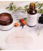 Økologiske hudplejeprodukter, inklusive en krukke med ansigtsmaske, en flaske serum, et gua sha-værktøj og Evolve Love Your Skin Trio på en marmoroverflade.
