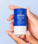 En person holder en COOLA Refreshing Water Stick SPF 50 - 22 g mod en lyseblå baggrund.