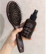 En hånd der holder en John Masters Organics Combo Paddle Brush - vildsvinehår og en flaske John Masters Organics leave-in conditioning mist.