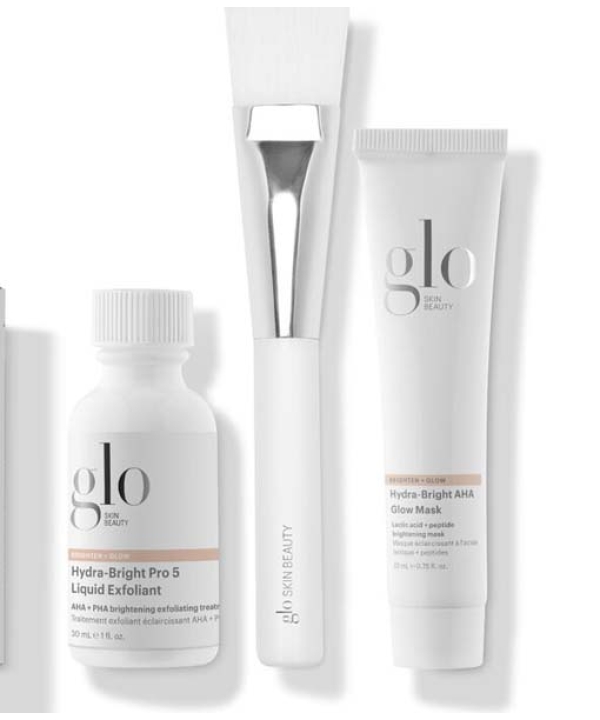 Three Glo Skin Beauty Radiant Spa Day Kit - Begrænsede hudplejeprodukter: en hvid flaske Hydra-Bright Pro 5 Liquid Exfoliant, en hvid tube Hydra-Bright AHA Glow Mask og en hvid påføringsbørste.