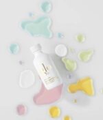 En hvid flaske mærket "Glo Hydra-Bright Pro 5 Liquid Exfoliant 60 ml" ligger midt mellem farverige væskestænk på en hvid overflade.