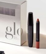 En sølv æske mærket "Glo Beauty Time To Shine - Warm Collection" sidder ved siden af en sort mascara tube og en rød læbe farveblyant.