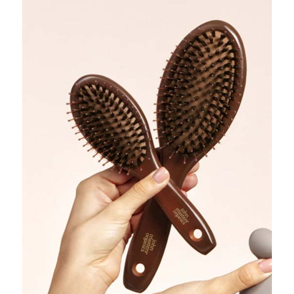 En person holder to John Masters Organics Combo Paddle Mini-børster med plastikbørster og håndtag, med branding-tekst.