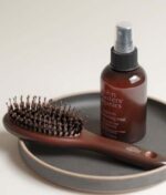 En John Masters Organics Combo Paddle Brush - Mini og en flaske John Masters Organics leave-in conditioning mist placeres på en rund, grå bakke.